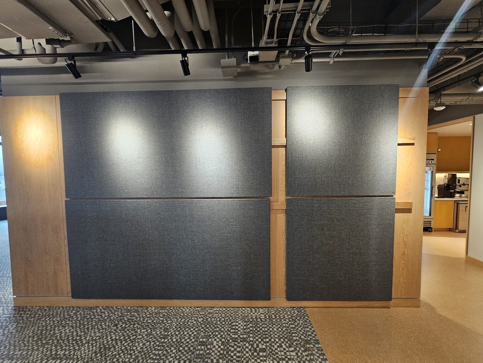 Four grey fabric boards in two rows set into an oak-panelled wall and lit by downlights, with the mounting rails visible between the panels