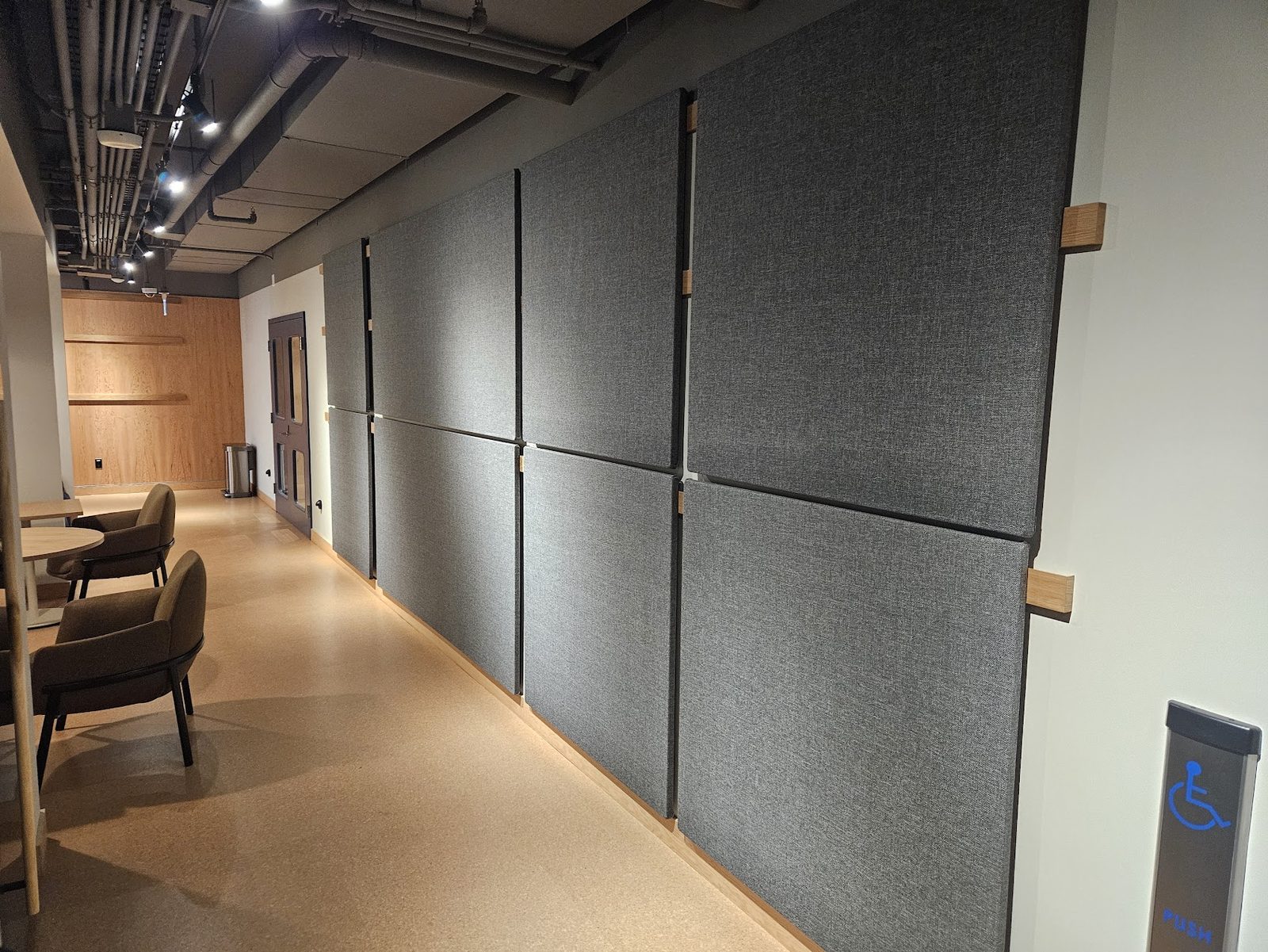 A corridor lined with six grey fabric CinemaBoards in two rows set edge to edge, with oak mounting rails visible on the white wall where the run ends