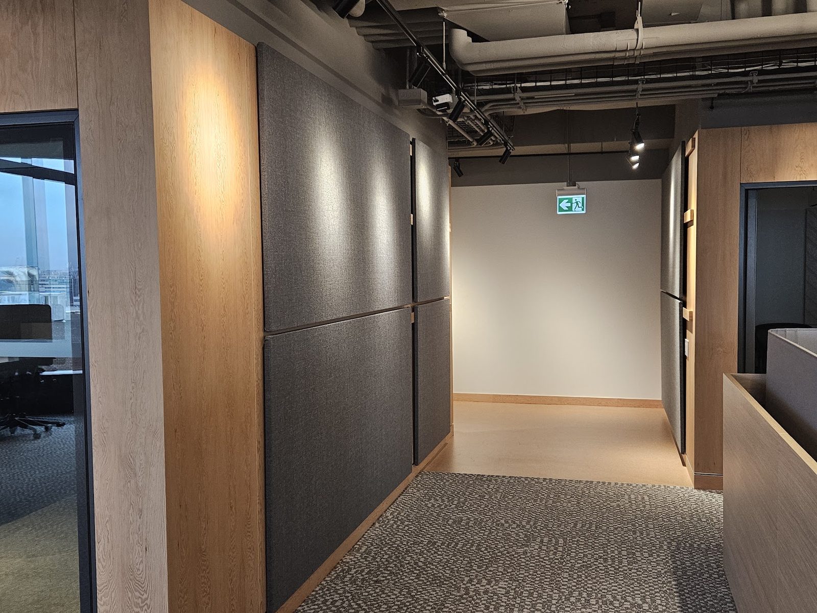 A run of grey fabric boards in two rows along an office corridor, meeting an oak-panelled wall at the corner