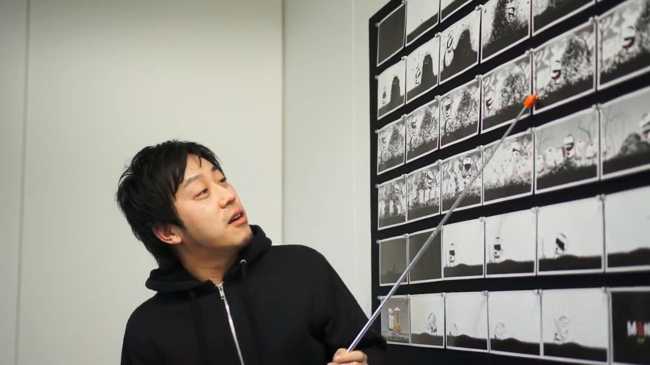 A person standing beside a CinemaBoard carrying a dense grid of small black and white storyboard frames in rows, using a long pointer to indicate one of them